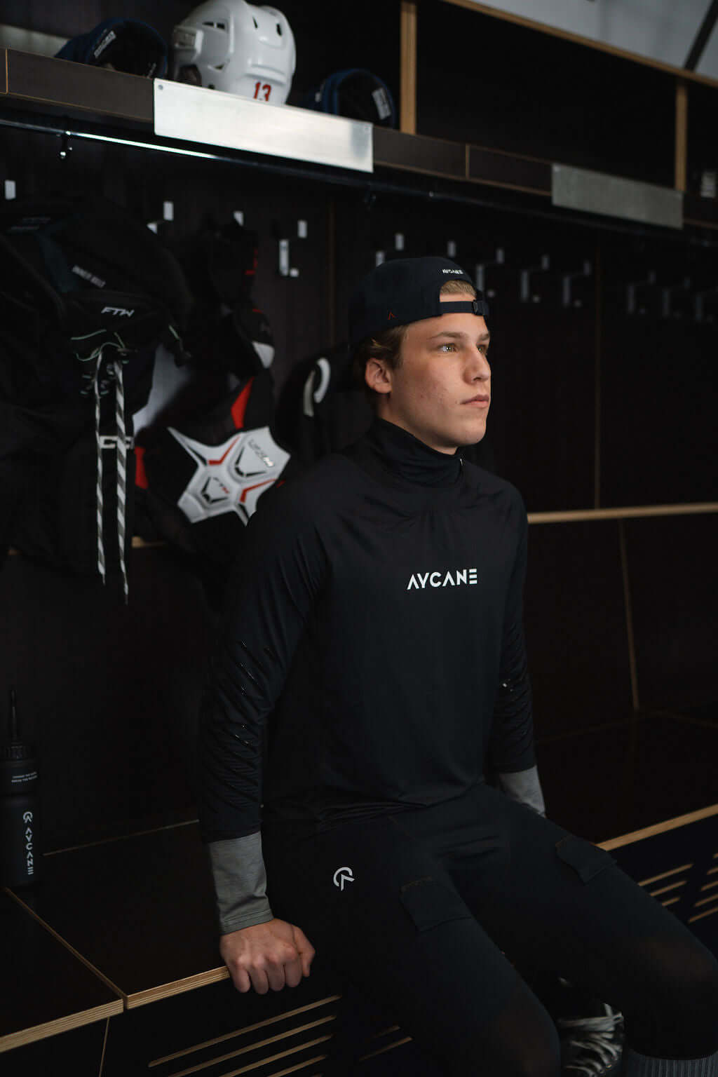 Young athlete wearing a black long sleeve base layer shirt, seated in a locker room, preparing for hockey.