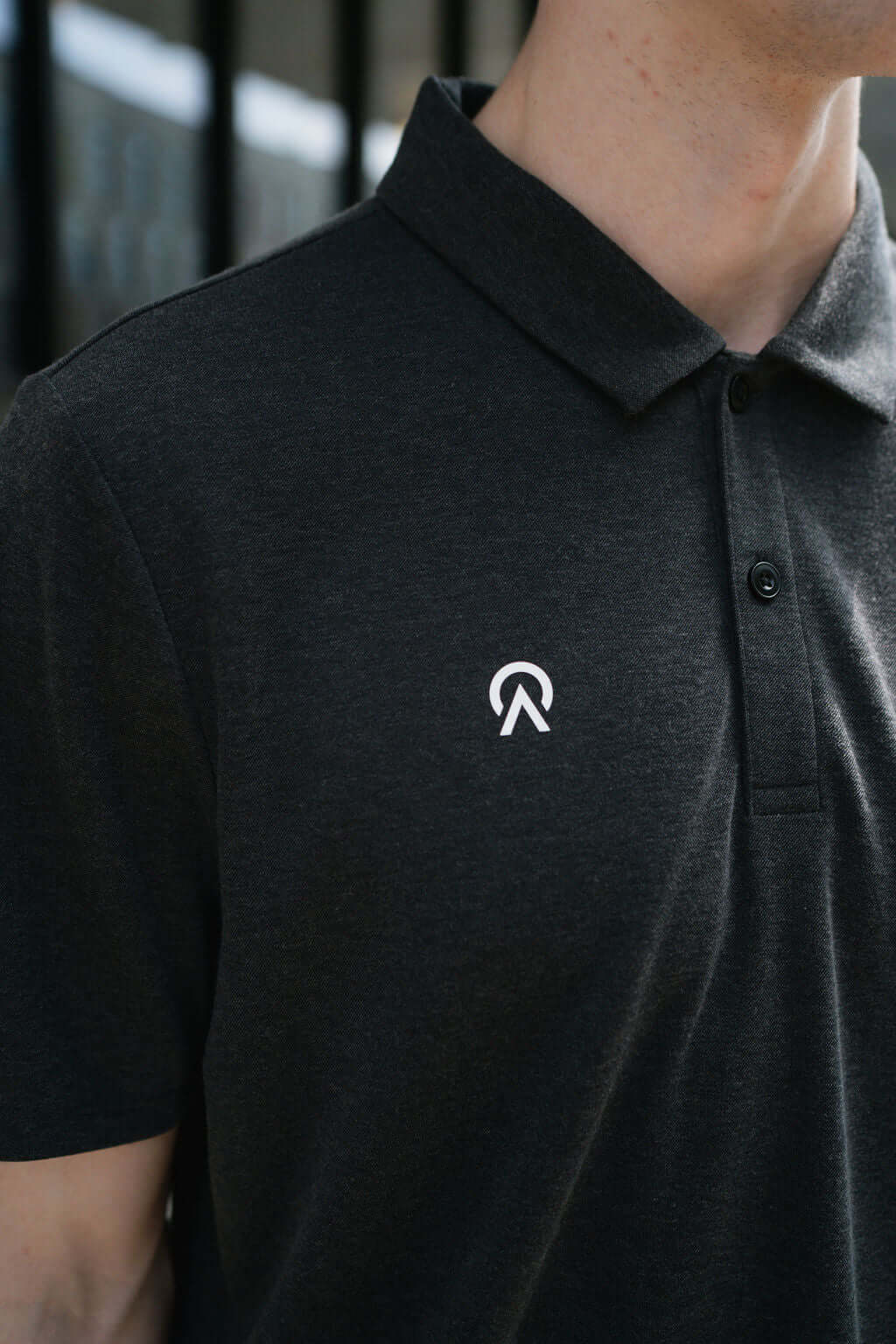 Close-up of a dark polo shirt featuring a white logo on the collar, showcasing stylish and modern apparel.