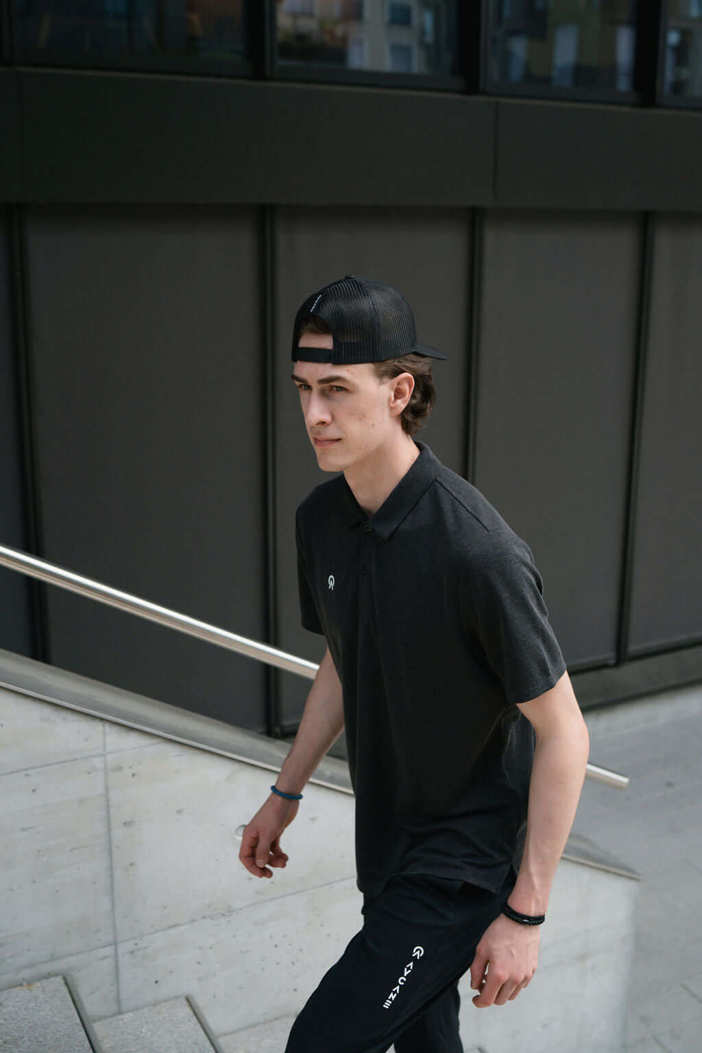 Young man wearing a black Netter Polo shirt and cap, walking down stairs in an urban environment.