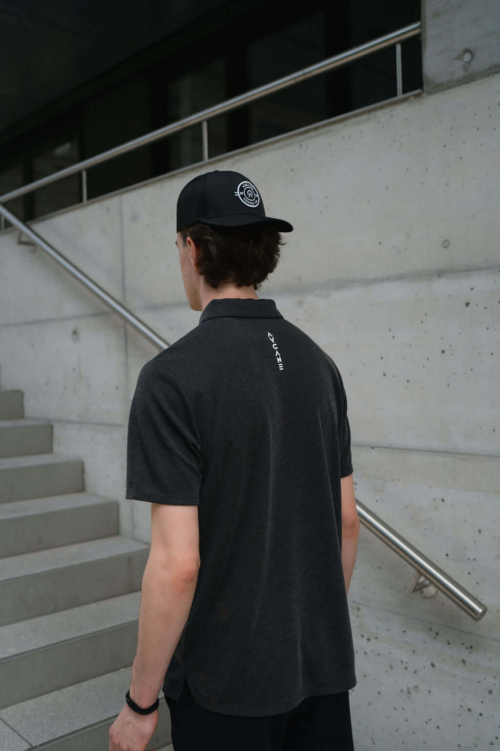 Back view of a man wearing a black Netter Polo shirt and cap, standing on outdoor stairs.