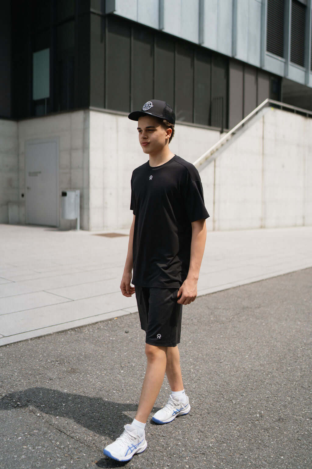 Young man in black Re.Force shorts and t-shirt walking outdoors on a stylish urban street.