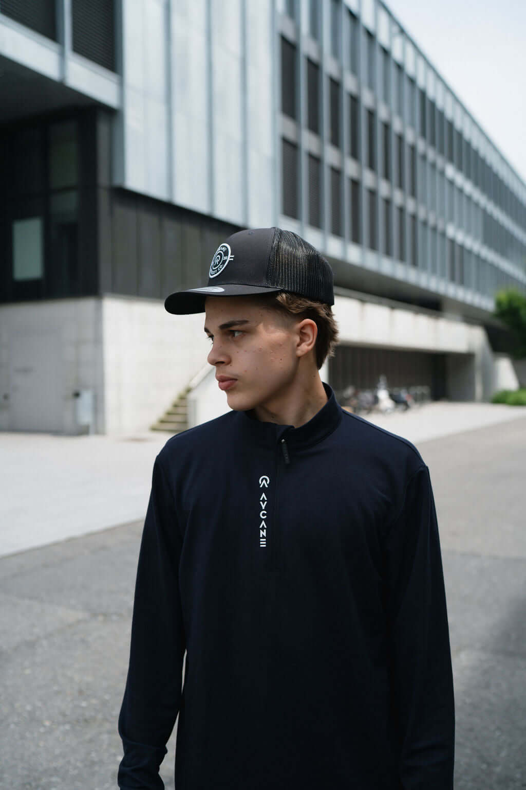 Young man wearing a black Maurize midlayer and a cap, standing outdoors in an urban setting.