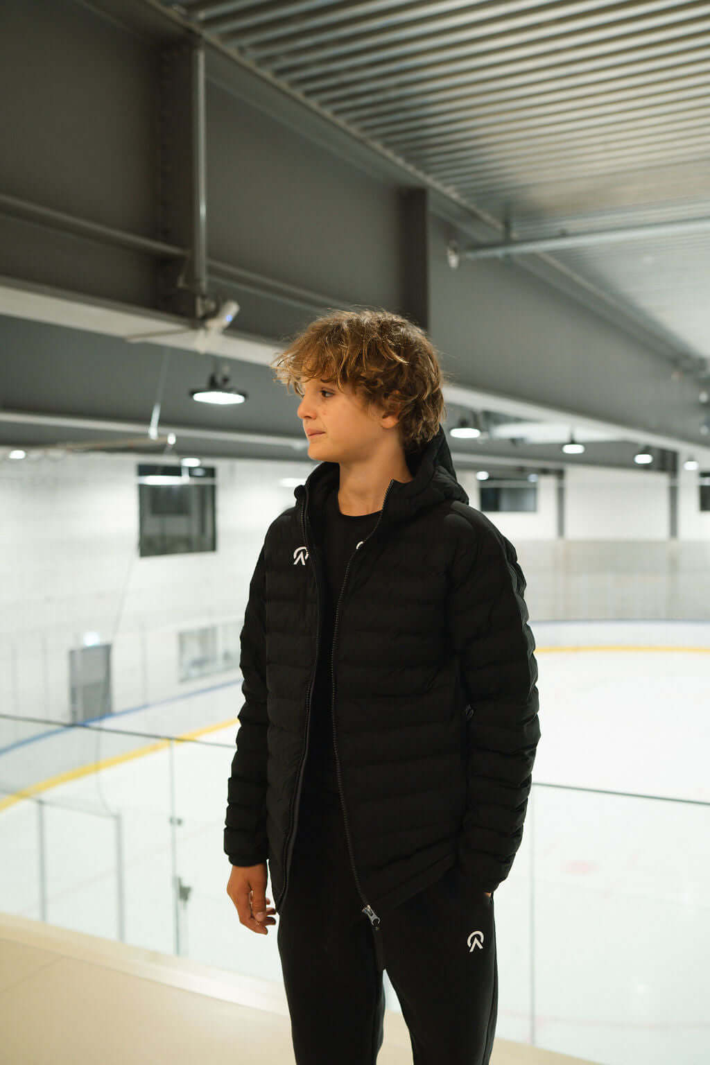 Young athlete wearing T-Lite Jacket in an ice rink, showcasing warmth and style in a sleek black design.