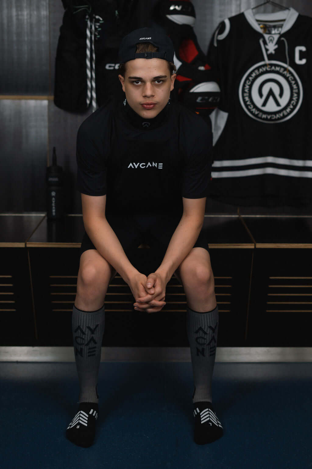 Young athlete wearing Blade X Base Layer Short Sleeve by BNQ, seated in locker room, showcasing cut-resistant athletic gear.