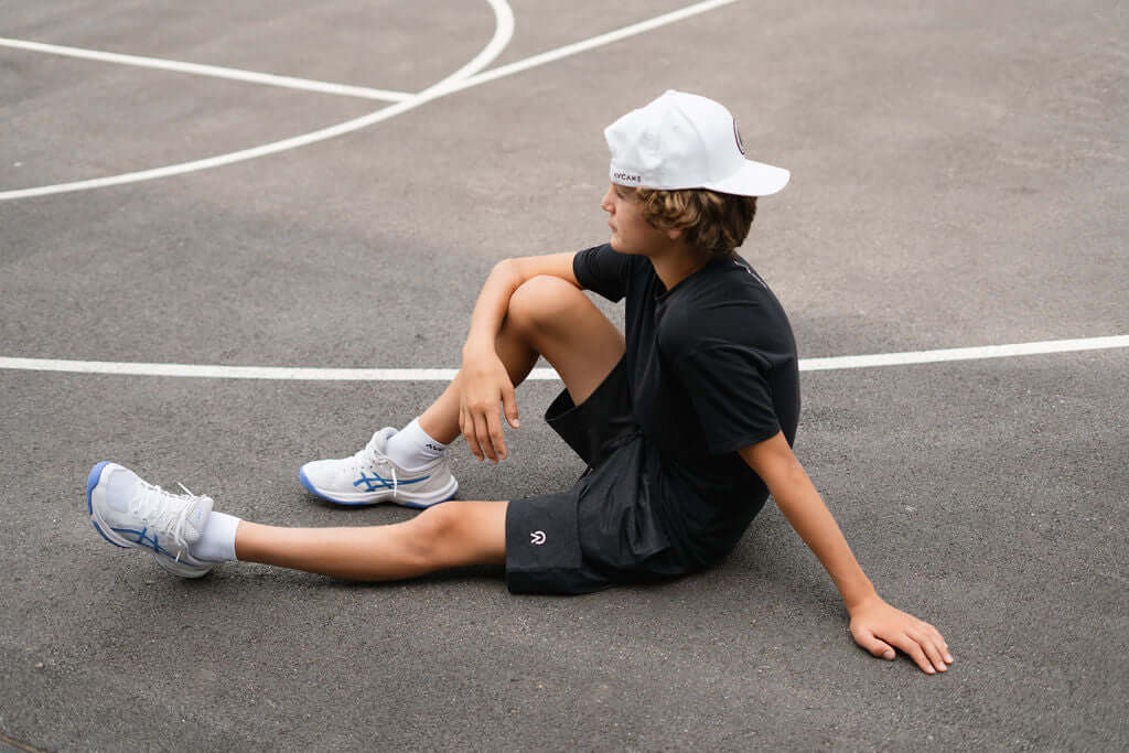 Boy wearing Re.Force Shorts and sneakers sitting on a basketball court, showcasing comfort and style.