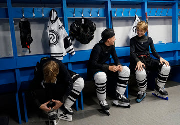 Youth competitive ice hockey players sitting shoulder to shoulder on the bench during an intense game, showing teamwork, focus, and shared struggle beyond winning.